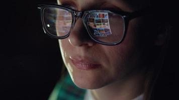kvinna i glasögon ser på de övervaka och surfing internet. de övervaka skärm är reflekterad i de glasögon video