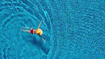 ver desde el parte superior como un mujer en un rojo traje de baño acostado en su espalda en el piscina. relajante concepto video