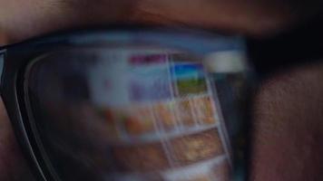 Woman in glasses looking on the monitor and surfing Internet. The monitor screen is reflected in the glasses video