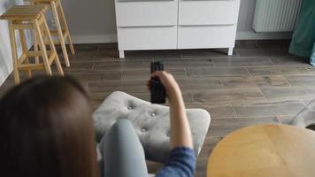 Woman is sitting in a chair, watching TV with a green screen, switching channels with a remote control. Chroma key video