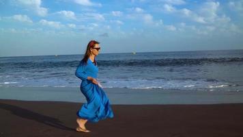 Portrait of a woman in a beautiful blue dress on a black volcanic beach. Slow motion video