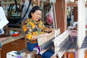 Asian women tourists try weaving with a hand loom in the concept of OTOP, community products, hand weaving fabrics, community shops, community weaving centers, community tourist attractions. photo