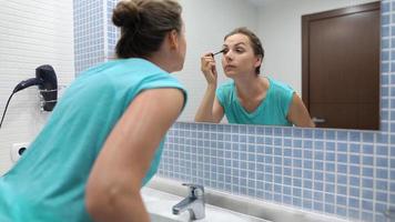 bonito mujer aplicando negro máscara para pestañas maquillaje en frente de baño espejo video