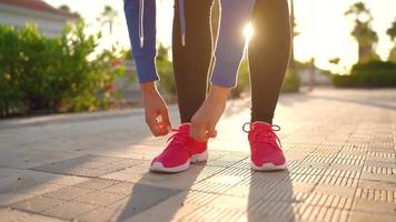 vicino su di donna legatura scarpa lacci e in esecuzione lungo il palma viale a tramonto video