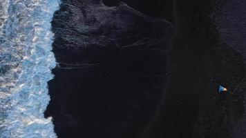 Top view of a girl in a blue dress and hat walking on the beach with black sand, foaming waves of the Atlantic Ocean. Tenerife, Canary Islands, Spain video