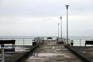 silhoutte de un solitario niña sentado en un banco en el muelle y mirando a el mar en nublado clima. foto