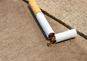 Broken cigarette close-up on a wooden table. No smoking or anti-smoking movement. A cigarette is broken on a wooden table and tobacco powder comes out. Cigarette-banned concept. photo