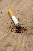 Cigarette burning on a wooden table. Cigarette with tobacco powder, burning on a wooden surface. Burning cigarettes with the smoke. Cigarette addiction and risk concept. Nicotine and tobacco close up. photo