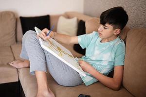 Young male teenager painting picture by numbers on canvas in living room at home. Hobby and leisure concept. photo