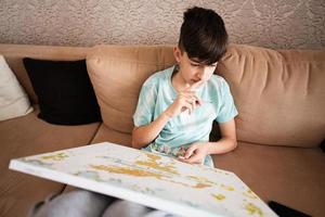 Young male teenager painting picture by numbers on canvas in living room at home. Hobby and leisure concept. photo