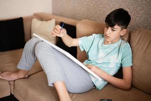 Young male teenager painting picture by numbers on canvas in living room at home. Hobby and leisure concept. photo