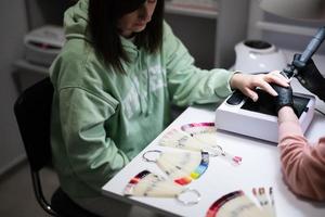 Manicure master working with female client in beauty salon. Woman chooses color of nail polish from palette. photo