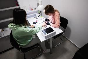 Manicure master working with female client in beauty salon. Manicurist makes woman nail. photo