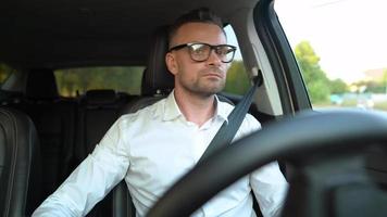 barbu homme dans des lunettes et blanc chemise conduite une voiture dans ensoleillé temps video