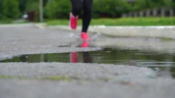 dichtbij omhoog van poten van een loper in sportschoenen. sport- vrouw jogging buitenshuis, stepping in modderig plas. single loper rennen in regenen, maken plons video