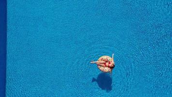 Visualizza a partire dal il superiore come un' donna nel un' rosso costume da bagno nuoto e dire bugie su sua indietro nel il piscina. rilassante concetto video