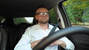 Bearded man in glasses and white shirt driving a car in sunny weather video