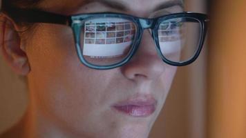 mulher dentro óculos olhando em a monitor e surfar Internet às noite. a monitor tela é refletido dentro a óculos video