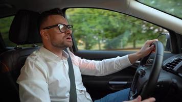 bärtig Mann im Brille und Weiß Hemd Fahren ein Auto im sonnig Wetter video