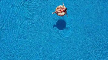 ver desde el parte superior como un mujer en un rojo traje de baño nadando y acostado en su espalda en el piscina. relajante concepto video