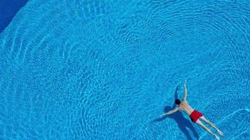 Aerial view of man in red shorts swims in the pool. Slow motion video