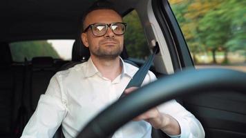 Bearded man in glasses and white shirt driving a car in sunny weather video