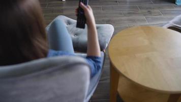 donna è seduta nel un' sedia, Guardando tv con un' verde schermo, commutazione canali con un' a distanza controllo. croma chiave video