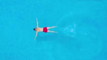 Aerial view of man in red shorts swims in the pool. Slow motion video