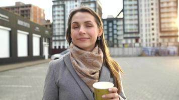 Portrait of a woman on a city background. Woman drinks coffee, turns around and leave video