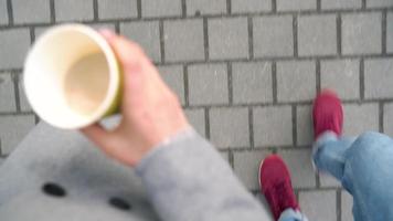 Top view of male and female legs strolling along the sidewalk. Woman drinking coffee video