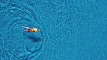 Visualizza a partire dal il superiore come un' donna nel un' rosso costume da bagno nuoto e dire bugie su sua indietro nel il piscina. rilassante concetto video