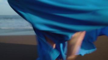 jambes de une femme dans magnifique bleu robe en marchant le long de une noir volcanique plage video