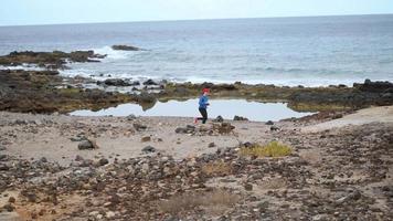 donna corre lungo il pietroso riva di il oceano. salutare attivo stile di vita. lento movimento video