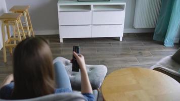 donna è seduta nel un' sedia, Guardando tv con un' verde schermo, commutazione canali con un' a distanza controllo. croma chiave video