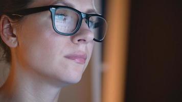 mujer en lentes mirando en el monitor y surf Internet a noche. el monitor pantalla es reflejado en el lentes video