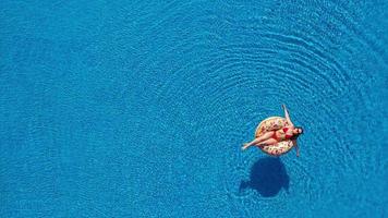 View from the top as a woman in a red swimsuit swimming and lying on her back in the pool. Relaxing concept video