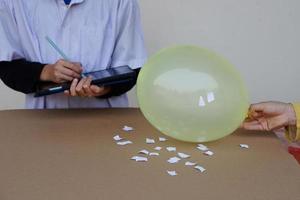 Closeup student do science experiment about static electricty from balloon and pieces of paper. Take note on smart tablet. Concept Science project work activity. Learning by doing. Education. photo