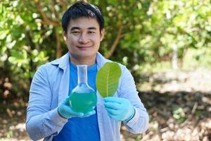 Asian man teacher do science experiment lesson outdoor. Nature color extract. Holds test bottle with green liquid inside and leaf. Concept, outdoor teaching and learning. science subject,Project work. photo