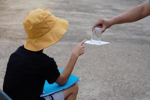 Student boy wears hat, hold book, learning science experiment about air pressure from glass of water which covered by paper. Concept, science subject activity, education. Learning by doing photo