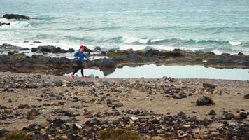 donna corre lungo il pietroso riva di il oceano. salutare attivo stile di vita video