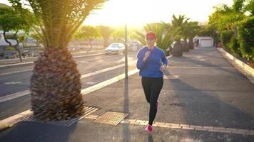 Woman tying shoelaces and starts jogging along the street among the tropical alley. Healthy active lifestyle video