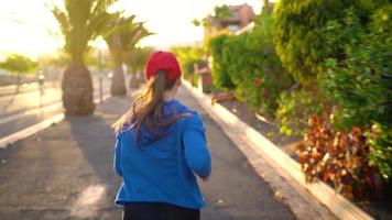 Woman tying shoelaces and starts jogging along the street among the tropical alley. Healthy active lifestyle video
