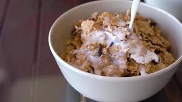 Tasty breakfast - milk is poured into a bowl with cornflakes and chocolate chips video