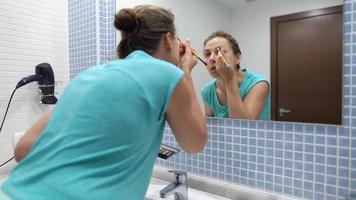 bonita mulher faz sobrancelha Maquiagem com olho sombra e Maquiagem escova dentro frente do banheiro espelho video