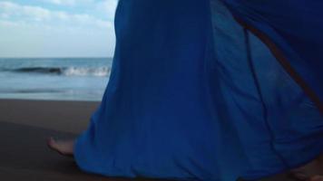 Legs of a woman in beautiful blue dress walking along a black volcanic beach video