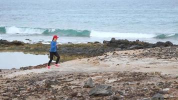 donna corre lungo il pietroso riva di il oceano. salutare attivo stile di vita. lento movimento video