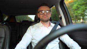 Bearded man in glasses and white shirt driving a car in sunny weather video