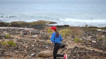 vrouw loopt langs de steenachtig kust van de oceaan. gezond actief levensstijl. langzaam beweging video