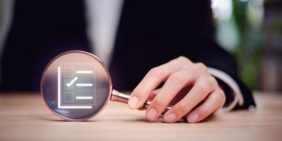 Businessman holding a magnifying glass and showing a marking concept on survey topic ,Auditing and evaluating the quality and efficiency of personnel ,Checklist with checkmarks and checkboxes photo