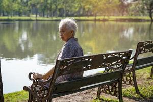 Asian elderly woman depressed and sad sitting back on bench in autumn park. photo